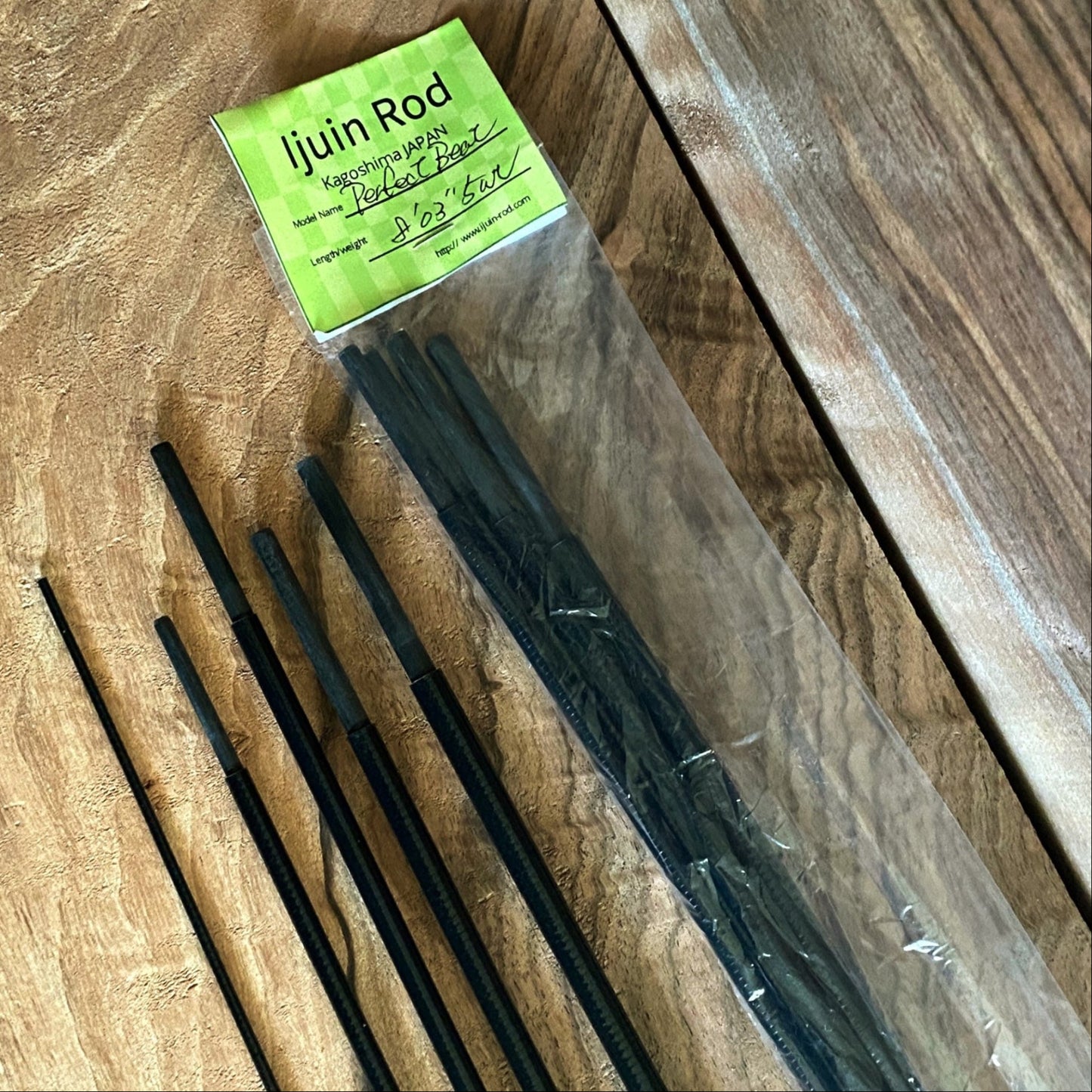 Packaged black rods with a green label on a wooden surface